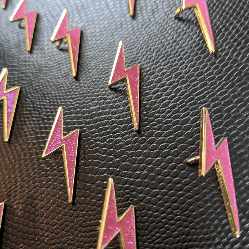 Pink and gold lightning bolt pins on a textured black surface