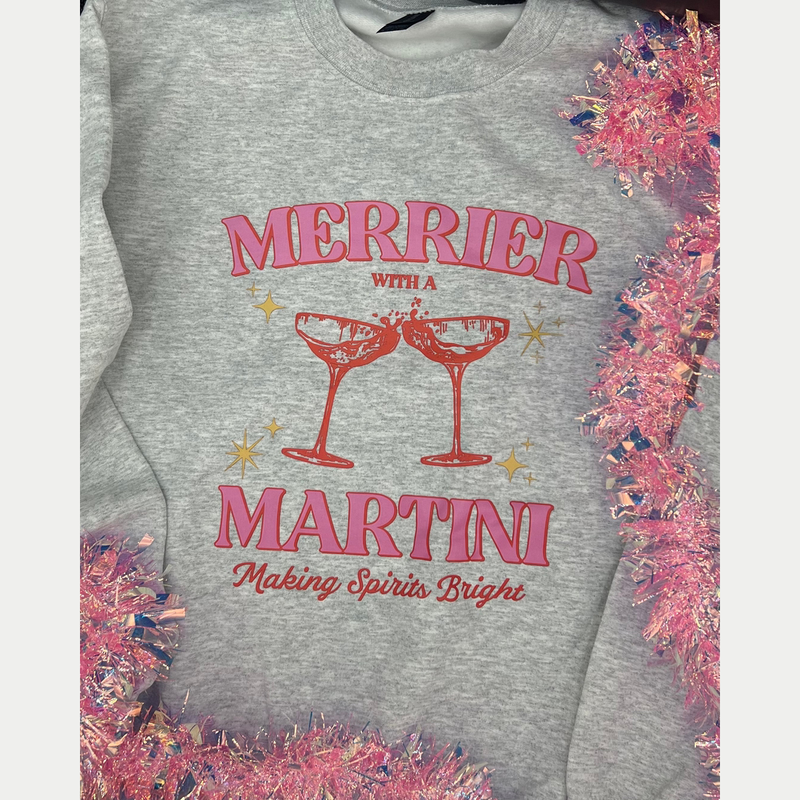 Gray Merrier With A Martini crewneck graphic with pink tinsel, shown in a square frame.