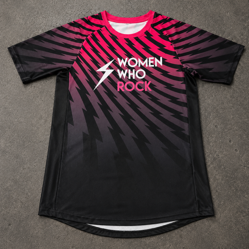 A short-sleeve athletic jersey laid flat on a gray textured surface. The shirt features a black base with a pink-to-purple-to-black gradient and diagonal lightning-bolt pattern across the body and sleeves.