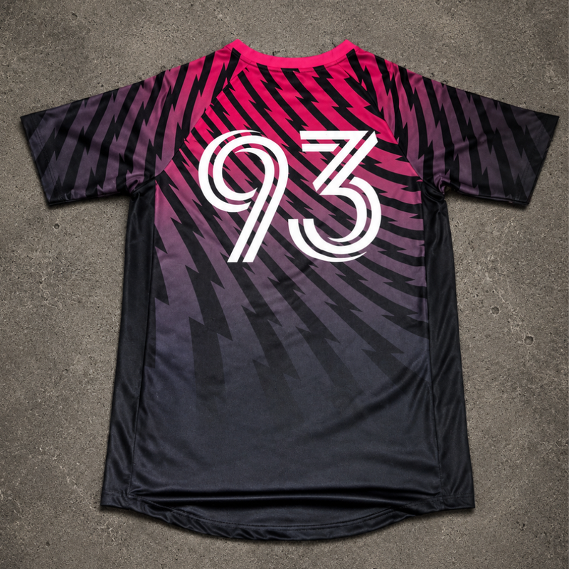 A short-sleeve athletic jersey laid flat on a gray concrete surface. The back of the shirt features a black-to-purple-to-pink gradient with diagonal striped patterns and a large white number '93' printed across the center.